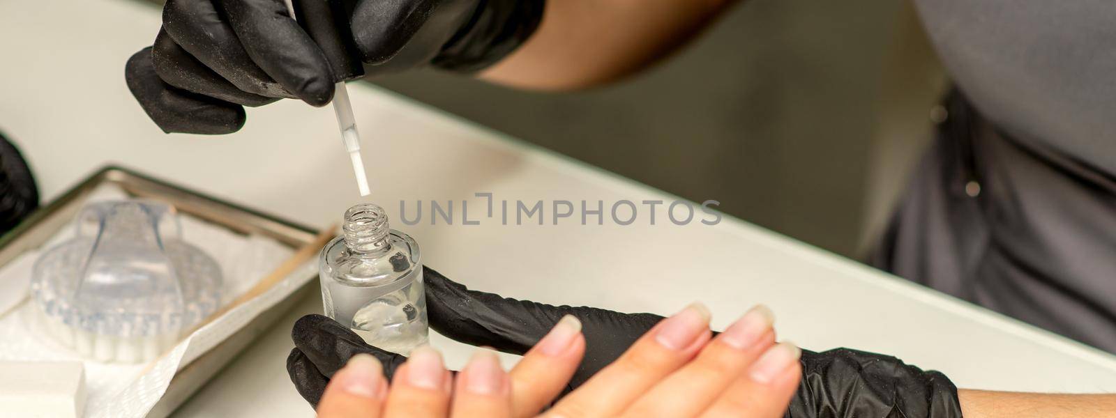 Manicure painting process. Manicure master paint the nails with transparent varnish in a nail salon, close up. by okskukuruza