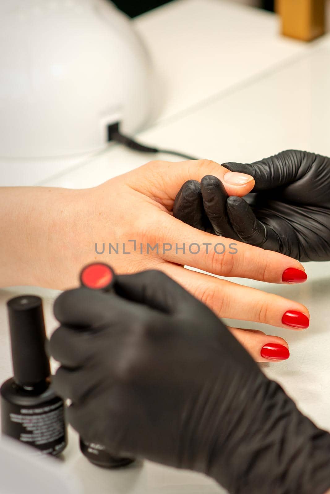 Professional manicure. A manicurist is painting the female nails of a client with red nail polish in a beauty salon, close up. Beauty industry concept. by okskukuruza