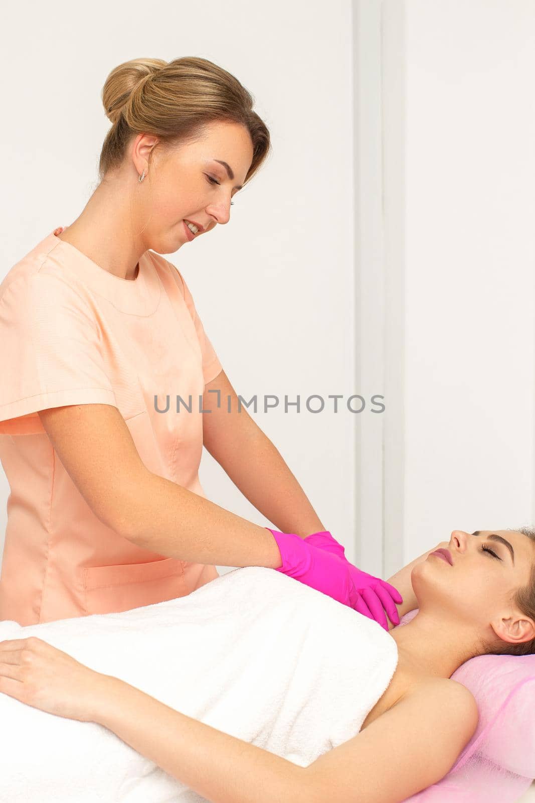 Beautician with a patient during sugaring. The cosmetologist waxes the female armpit