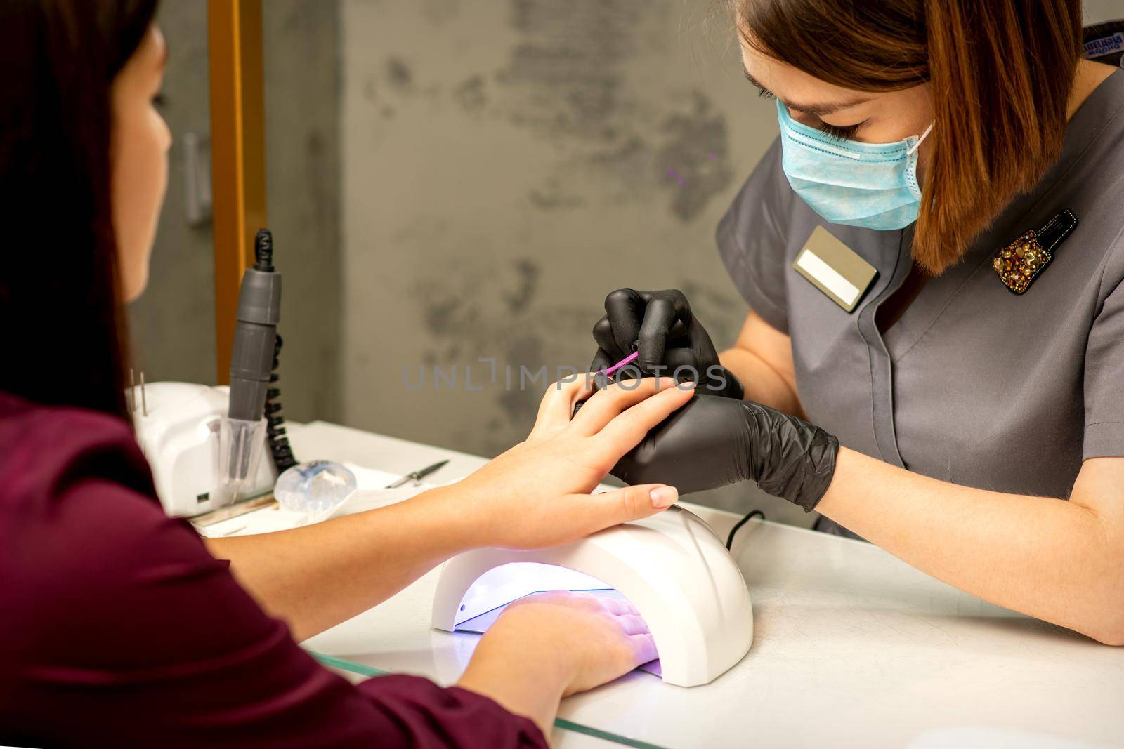 Professional manicure. A manicurist is painting the female nails of a client with purple nail polish in a beauty salon, close up. Beauty industry concept