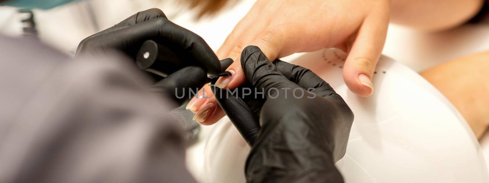Manicure painting process. Manicure master paint the nails with transparent varnish in a nail salon, close up. by okskukuruza