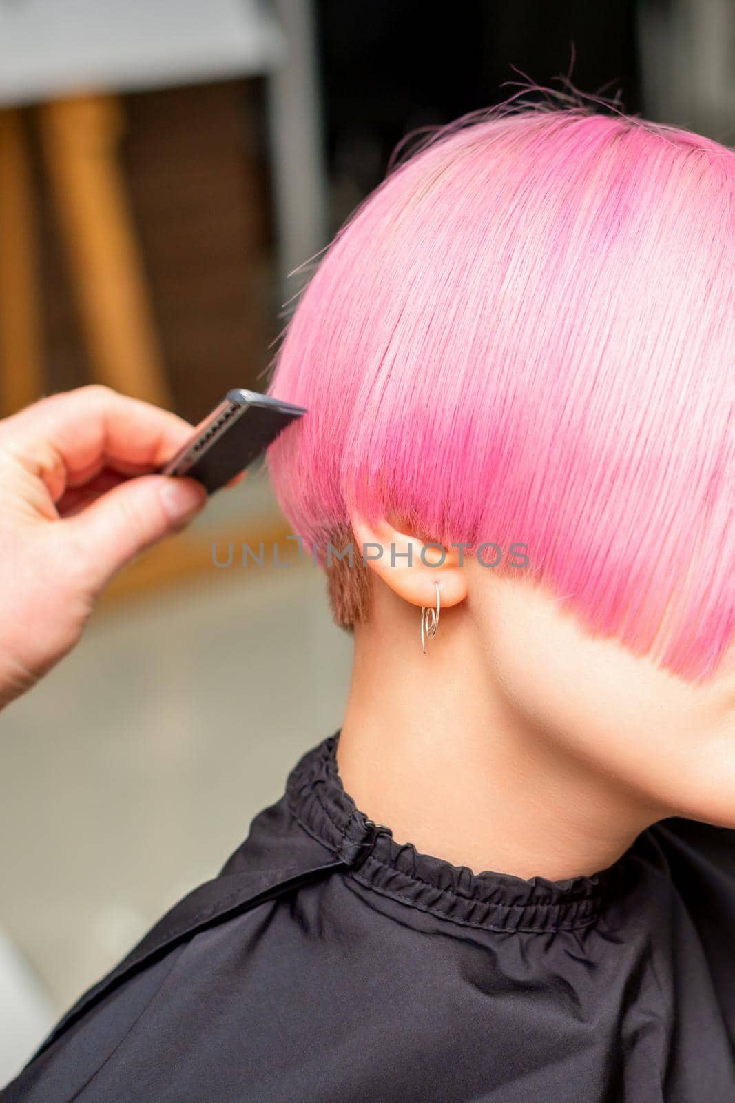 A hairdresser is combing the dyed pink short hair of the female client in a hairdresser salon