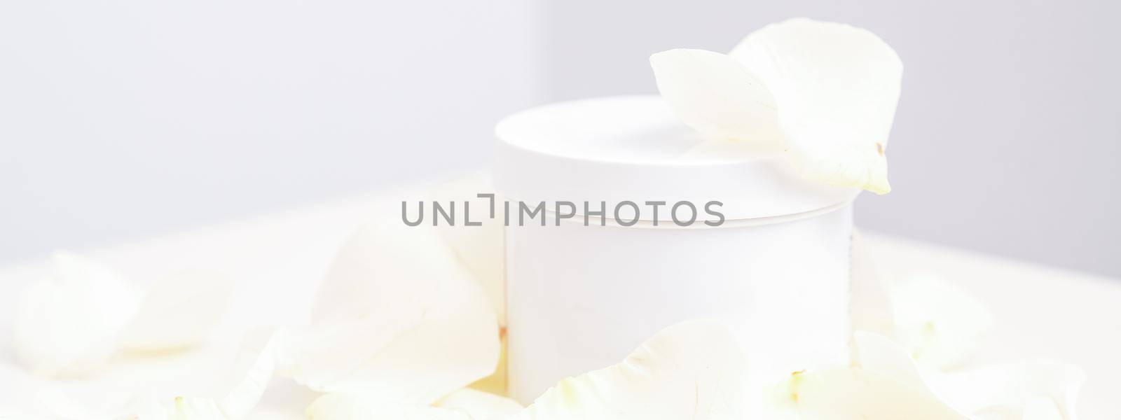 White jar with cream among delicate white rose flowers petals on a light background. Natural organic cosmetics concept, close up, mock-up