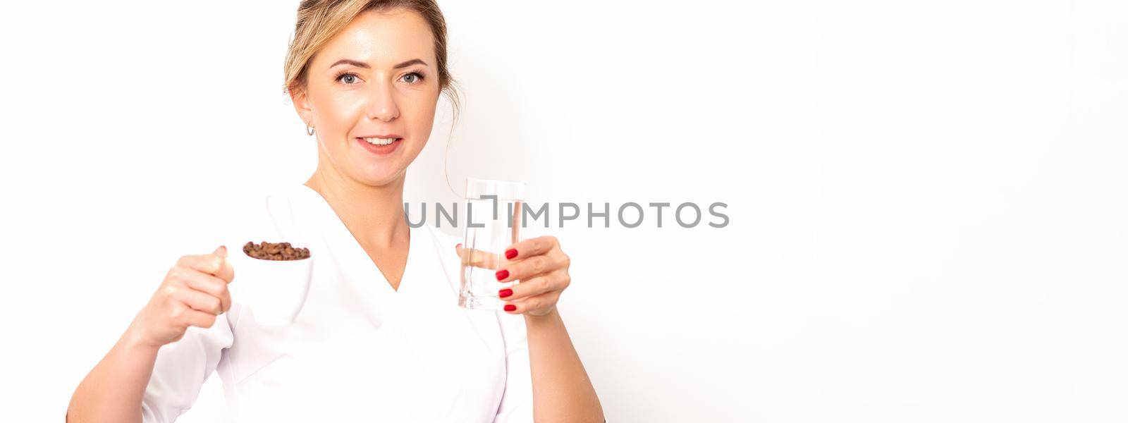 Coffee with water. The female nutritionist holds a cup of coffee beans and a glass of water in her hands on white background