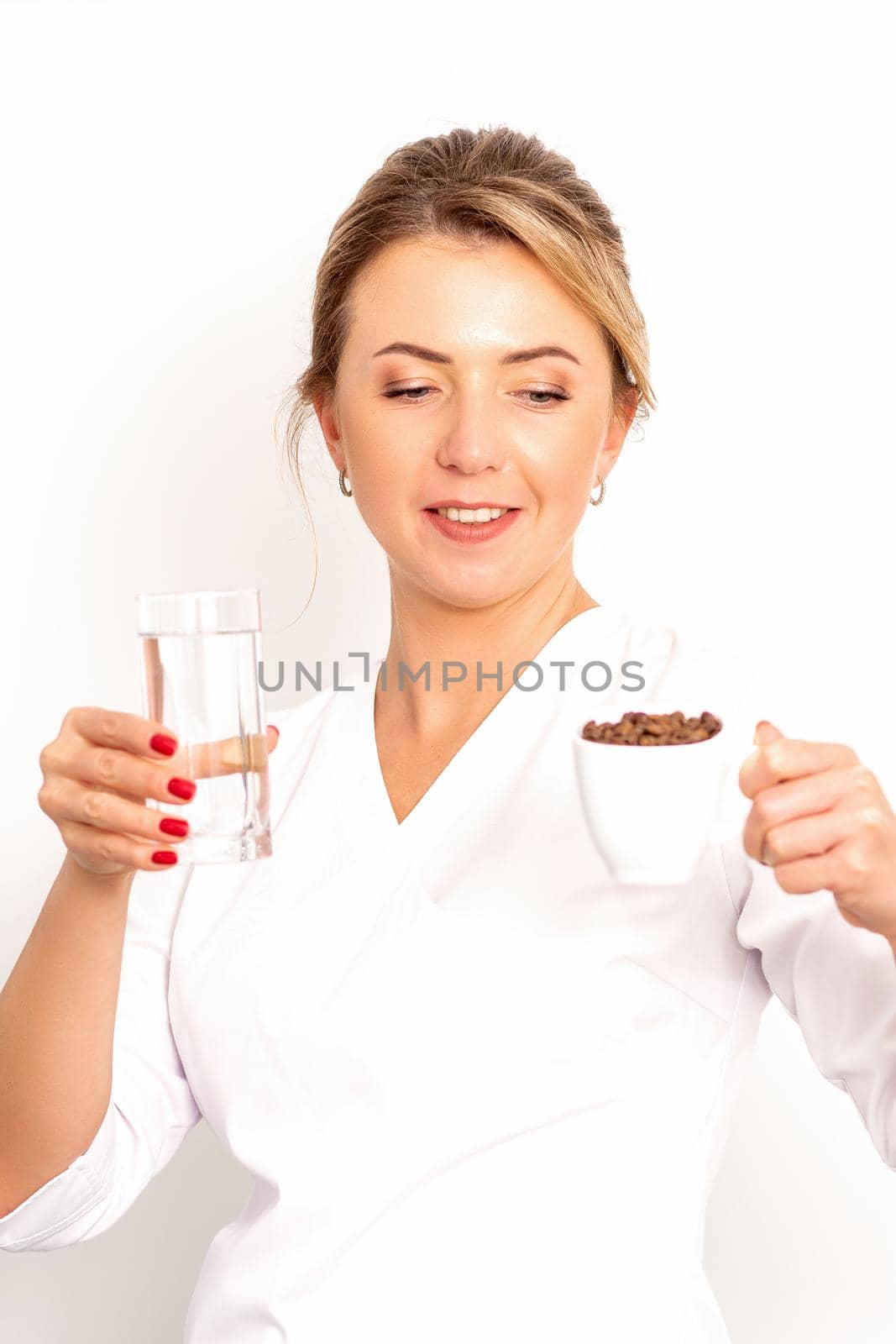Coffee with water. The female nutritionist holds a cup of coffee beans and a glass of water in her hands on white background. by okskukuruza