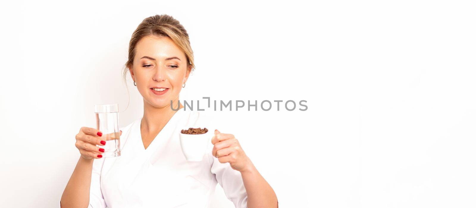 Coffee with water. The female nutritionist holds a cup of coffee beans and a glass of water in her hands on white background