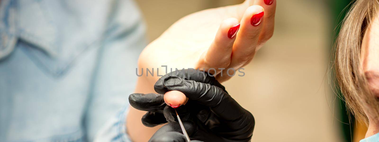 Professional manicure. A manicurist is painting the female nails of a client with red nail polish in a beauty salon, close up. Beauty industry concept. by okskukuruza