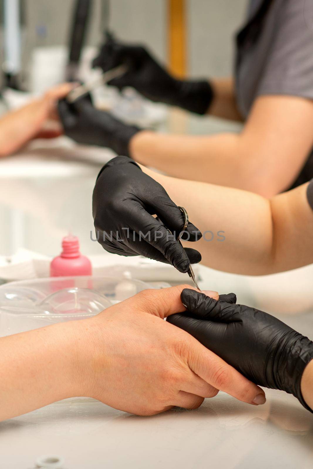 Manicure master removes cuticles from female nails with scissors wearing protective gloves in manicure salon. by okskukuruza