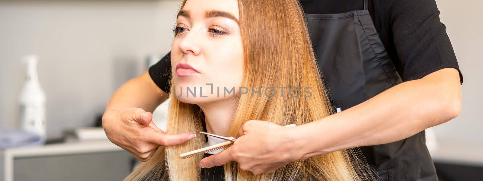 Beautiful young blonde woman with long straight blonde hair getting a haircut at the hairdresser salon. by okskukuruza