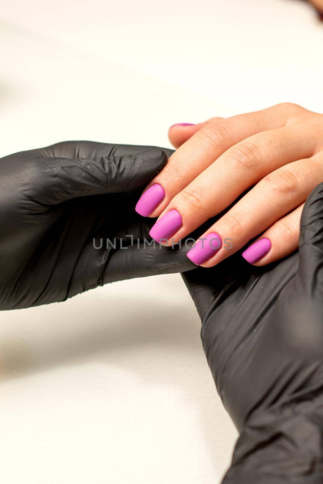 A manicurist holds beautiful young female hands showing finished purple, pink polish manicure in a nail salon. by okskukuruza