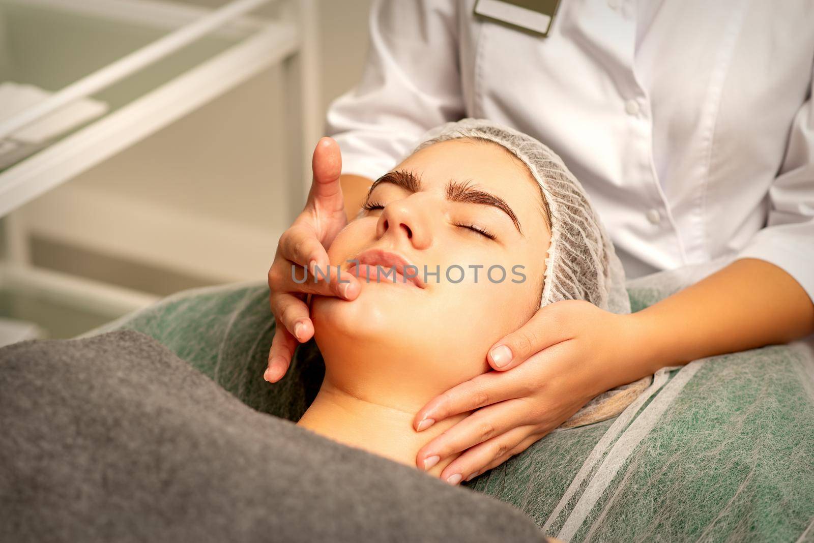 Face massage. Beautiful caucasian young white woman having a facial massage with closed eyes in a spa salon