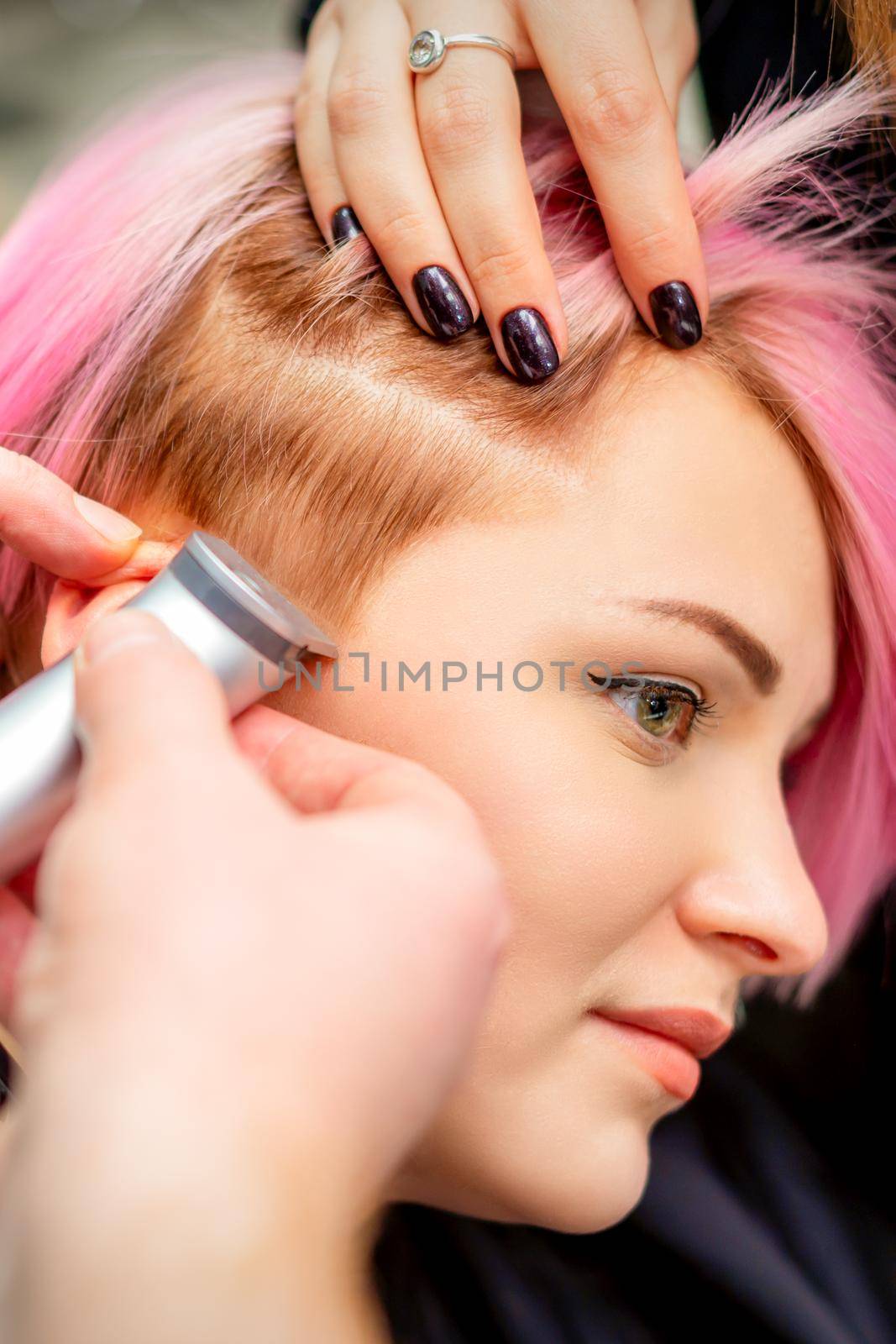 Hairdresser shaves female temple with pink hair by electric shaver in a hairdresser salon, close up. by okskukuruza