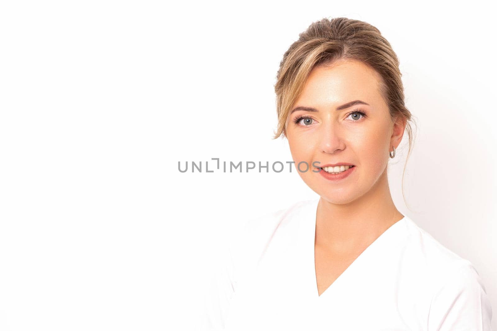 Close-up portrait of young smiling female caucasian healthcare worker standing staring at the camera on white background