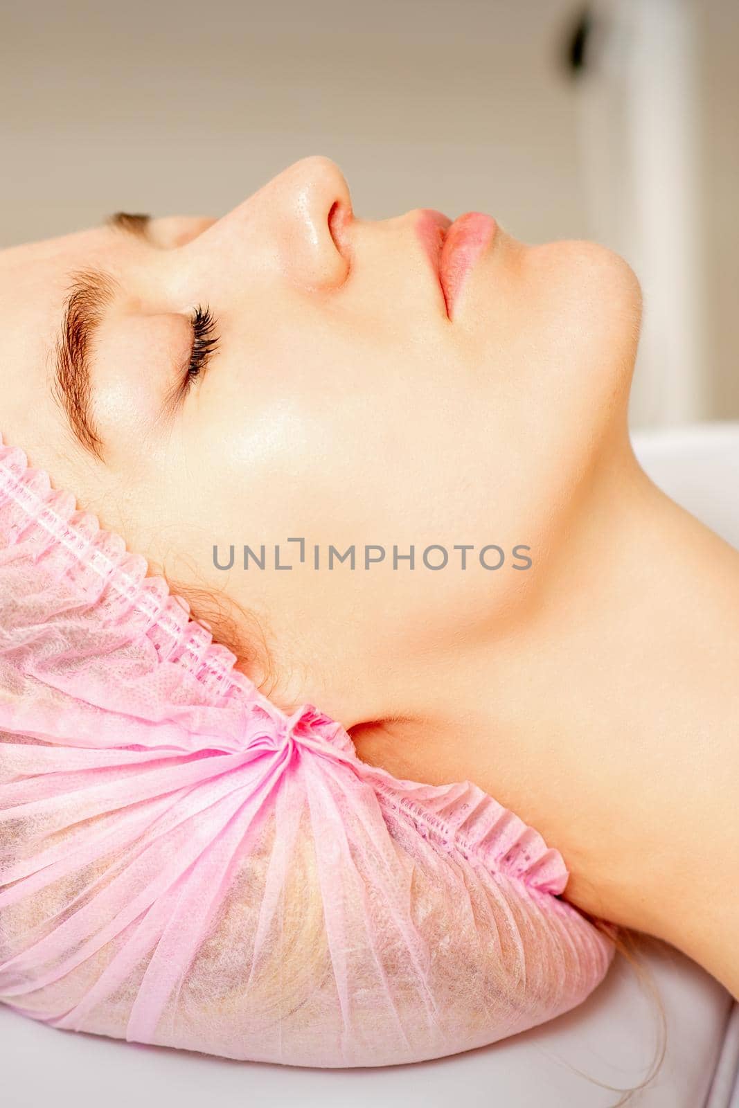 Side view of a young caucasian woman in a medical cap lying with closed eyes waiting for the cosmetic procedure in a beauty salon
