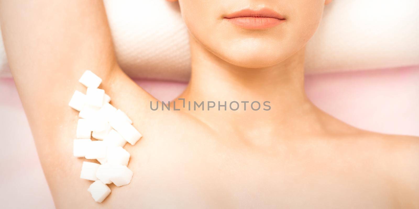 Sugaring, waxing concept. White sugar cubes lie down on the female armpit of the young white woman, close up