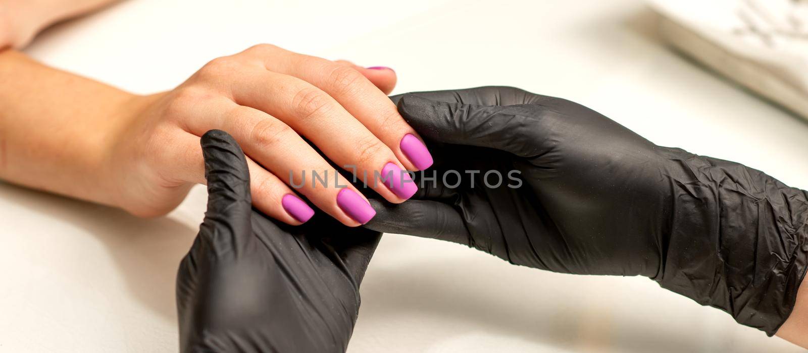 A manicurist holds beautiful young female hands showing finished purple, pink polish manicure in a nail salon