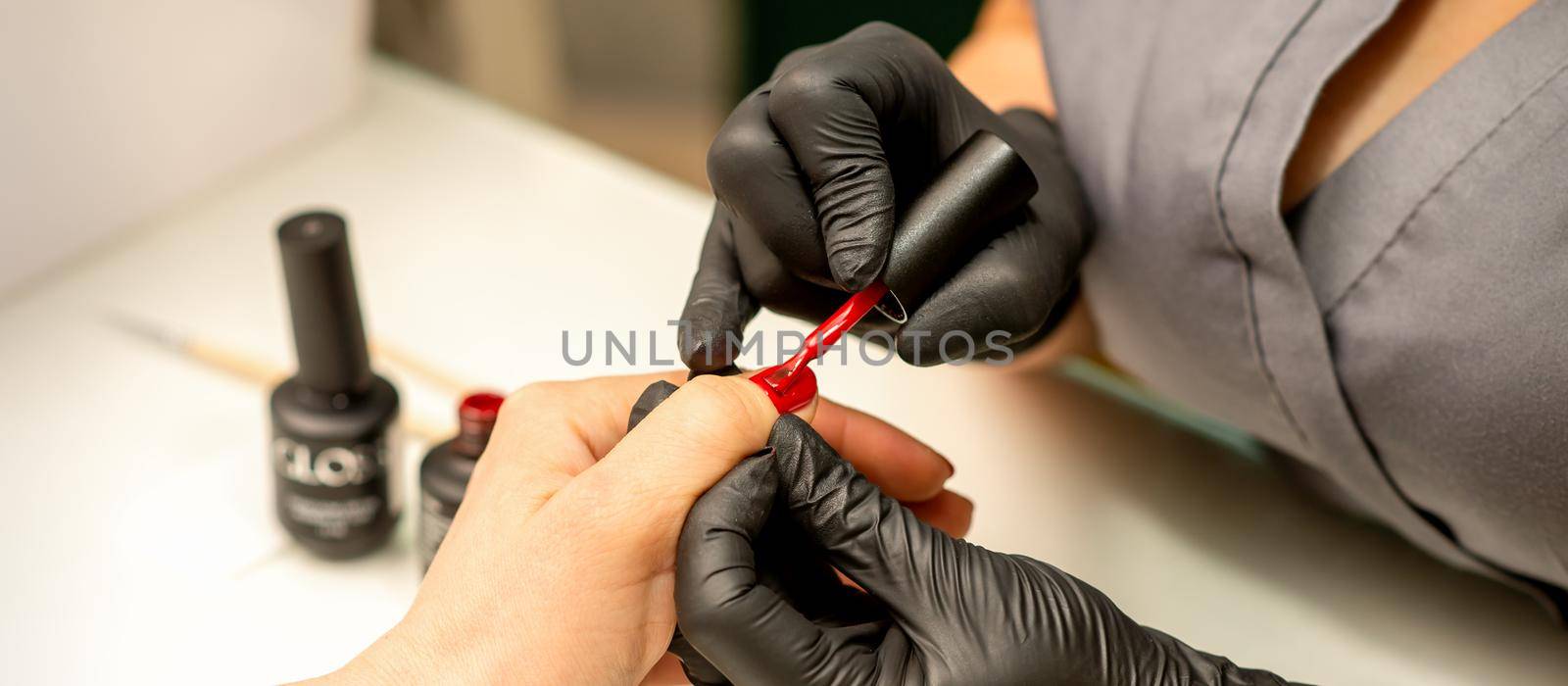 Professional manicure. A manicurist is painting the female nails of a client with red nail polish in a beauty salon, close up. Beauty industry concept