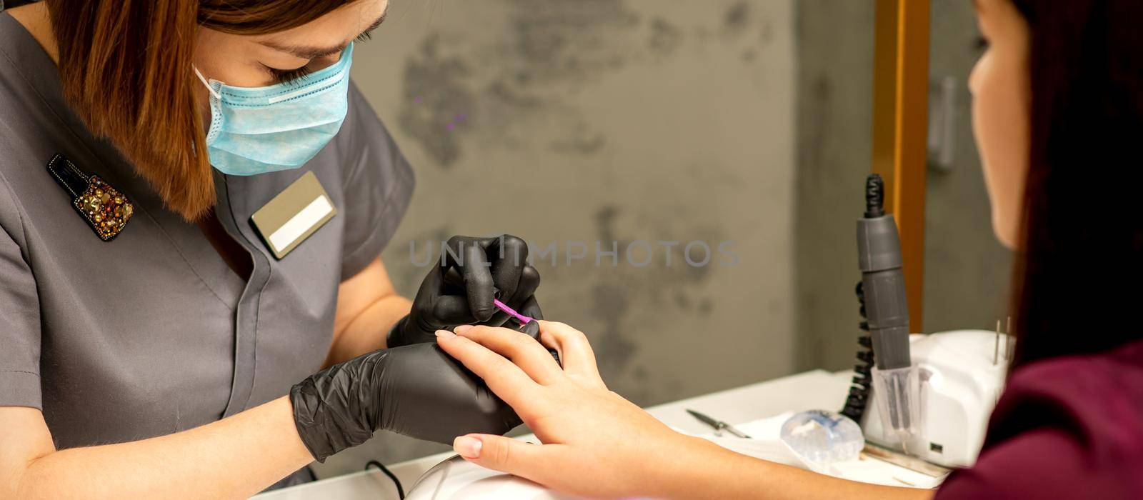 Professional manicure. A manicurist is painting the female nails of a client with purple nail polish in a beauty salon, close up. Beauty industry concept. by okskukuruza