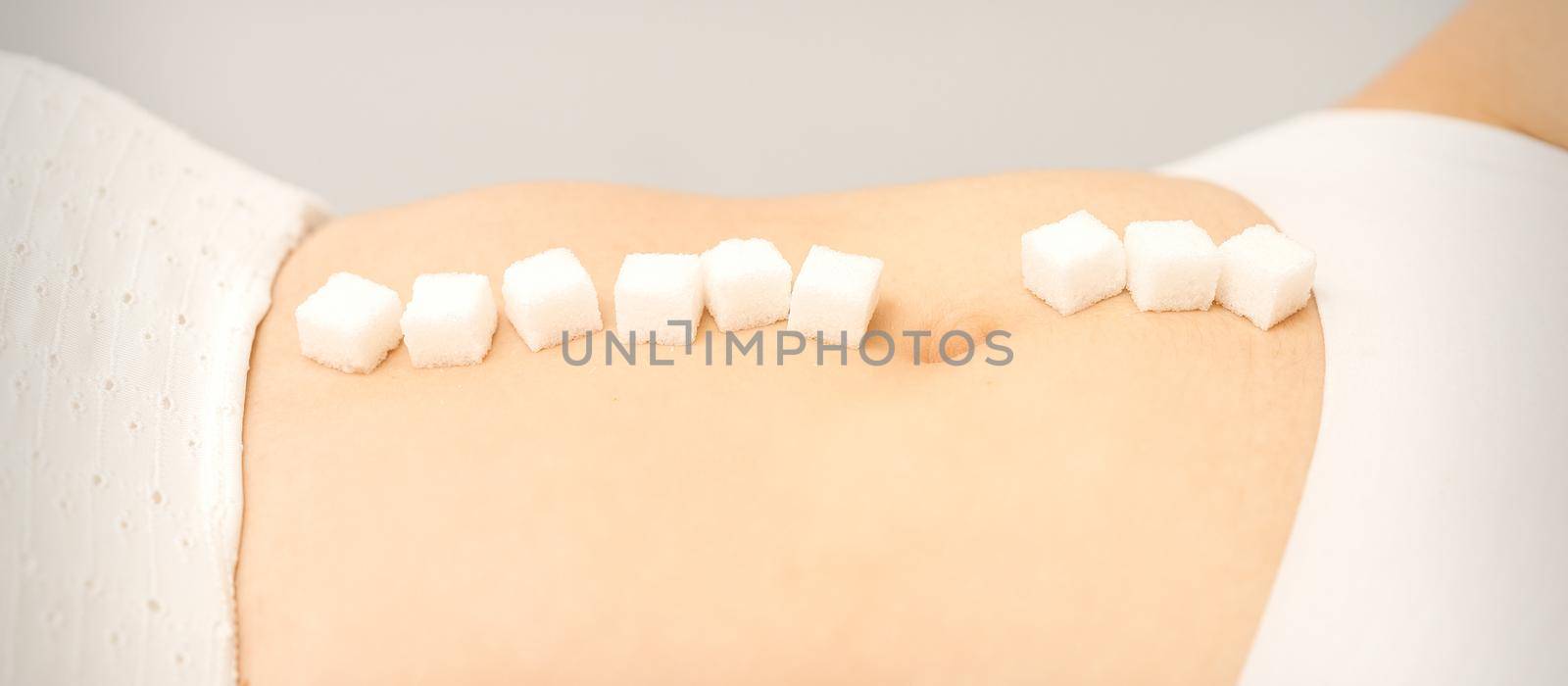 The concept of epilation, waxing. Sugar cubes lying in a row on the abdomen of a young white woman, close up
