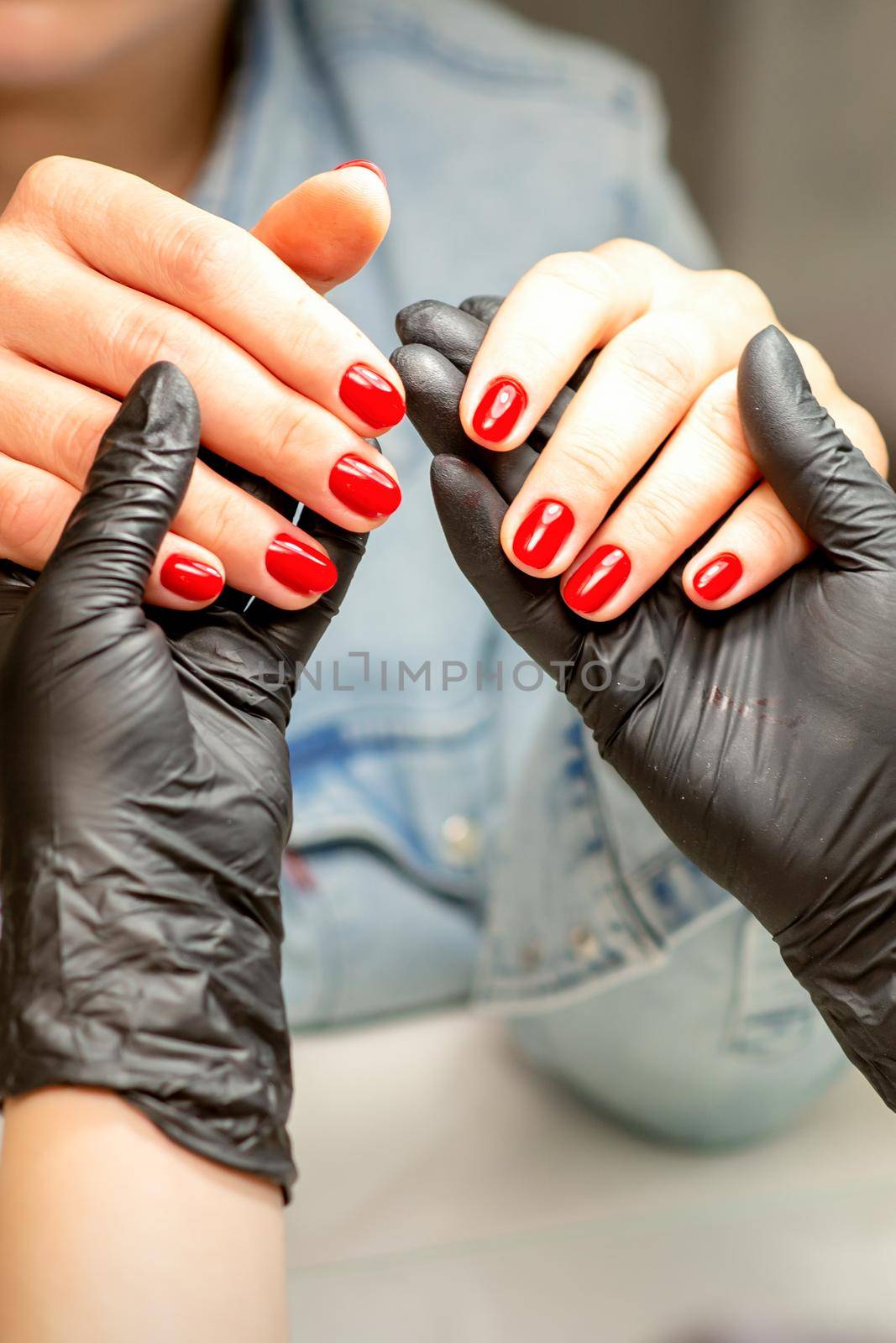 A manicurist holds beautiful young female hands showing finished red polish manicure in a nail salon. by okskukuruza