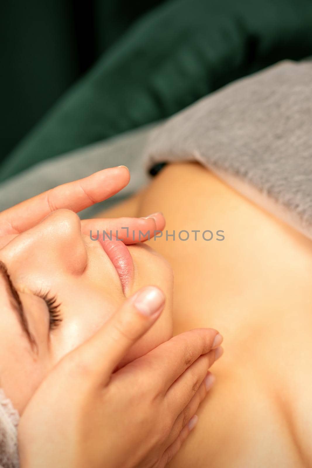 Beautiful young caucasian woman with closed eyes receiving a facial massage in a beauty salon