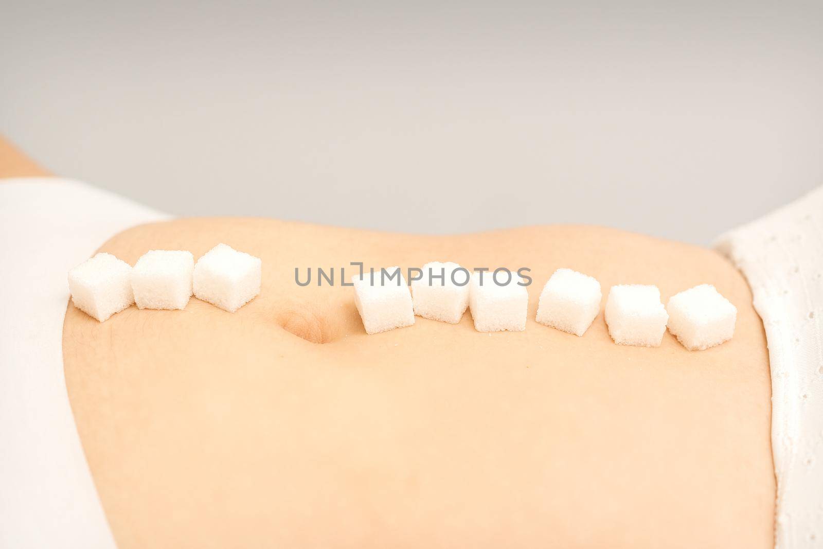 The concept of epilation, waxing. Sugar cubes lying in a row on the abdomen of a young white woman, close up. by okskukuruza