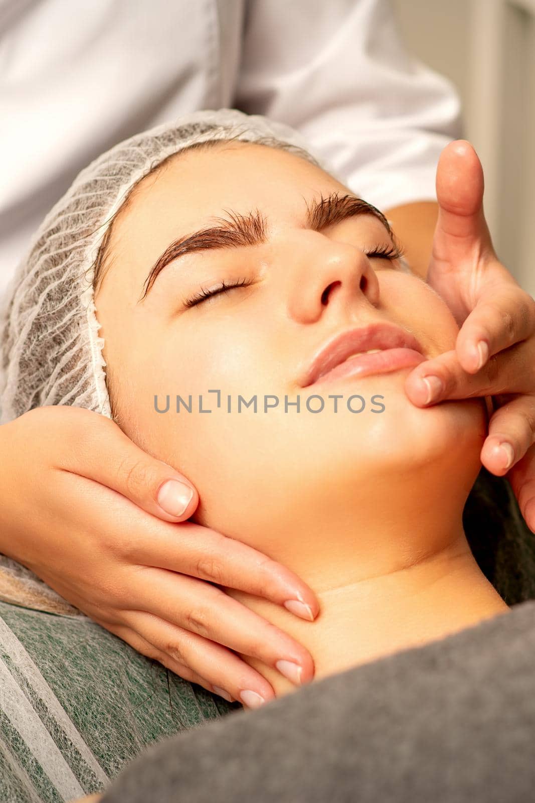 Face massage. Beautiful caucasian young white woman having a facial massage with closed eyes in a spa salon. by okskukuruza