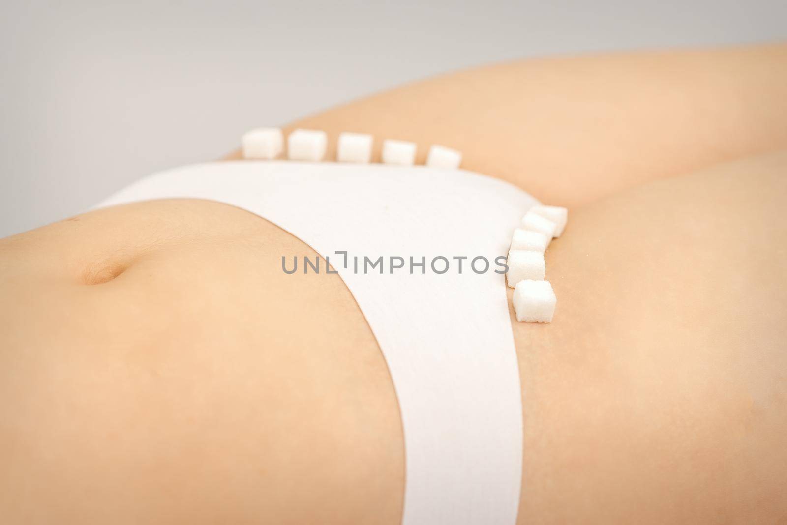 The concept of epilation, waxing, and intimate hygiene. Sugar cubes lying in a row on the bikini zone of a young white woman, close up