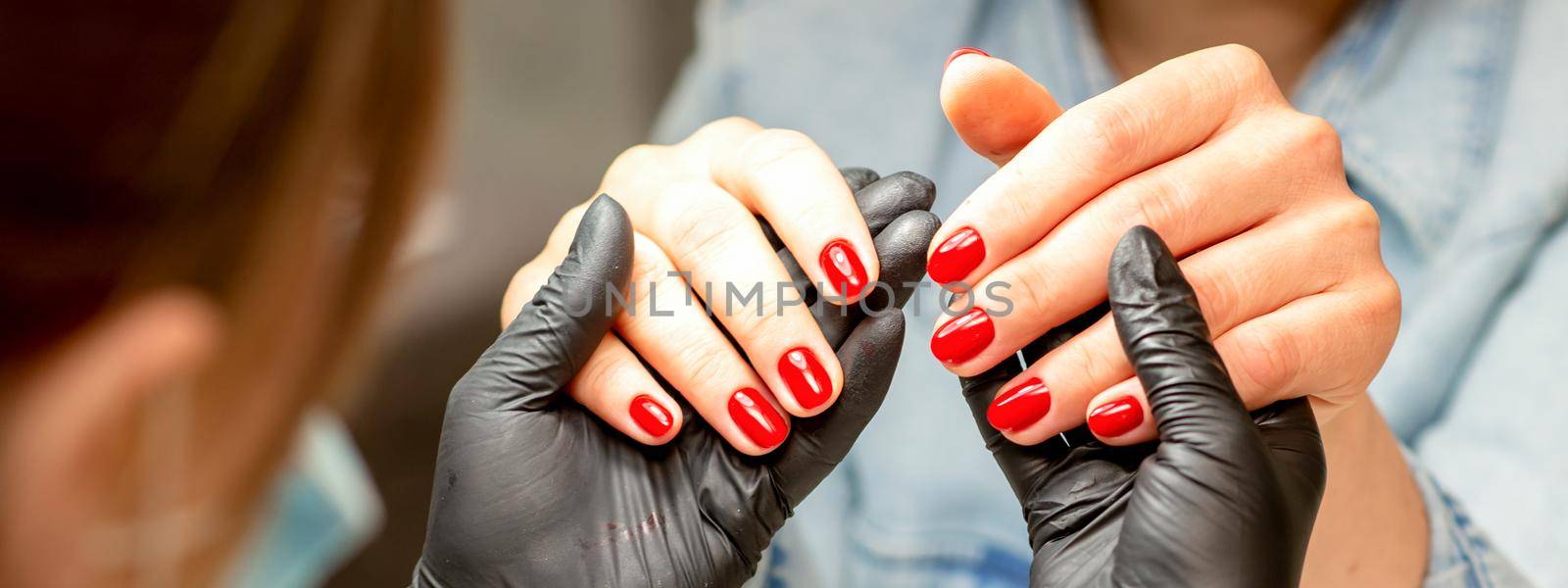 A manicurist holds beautiful young female hands showing finished red polish manicure in a nail salon. by okskukuruza