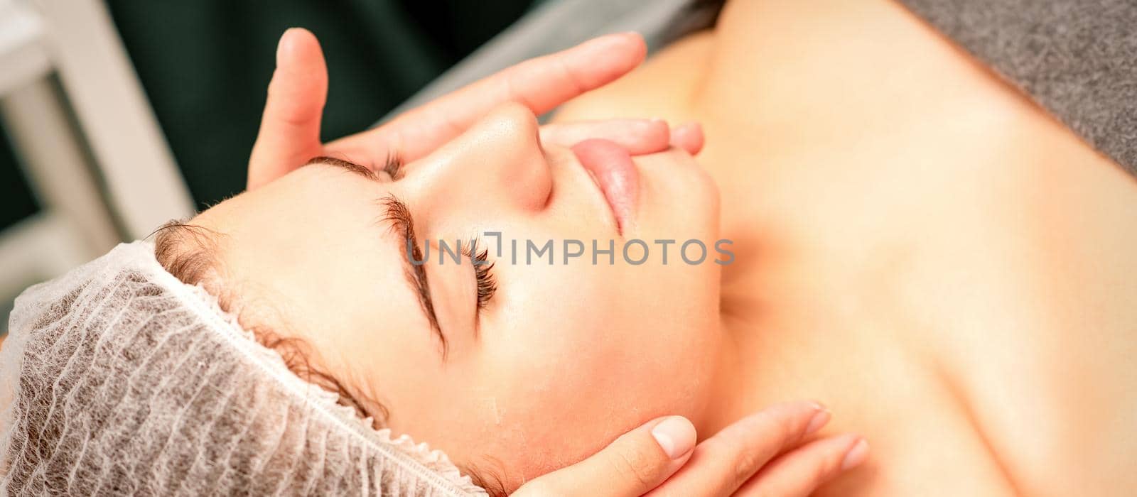 Face massage. Beautiful caucasian young white woman having a facial massage with closed eyes in a spa salon. by okskukuruza