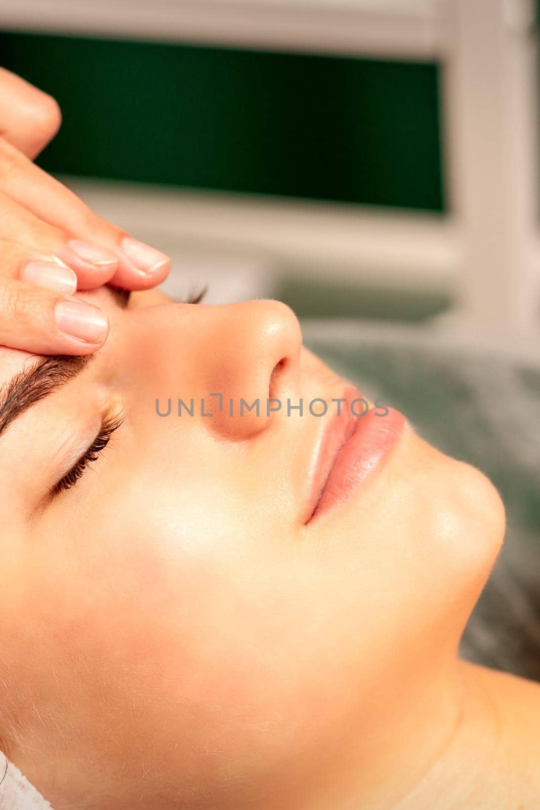 Head massage. Beautiful caucasian young white woman receiving a head and forehead massage with closed eyes in a spa salon. by okskukuruza