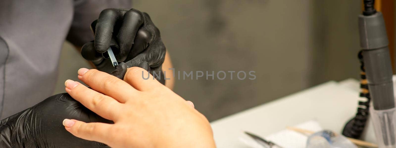 Manicure painting process. Manicure master paint the nails with transparent varnish in a nail salon, close up. by okskukuruza