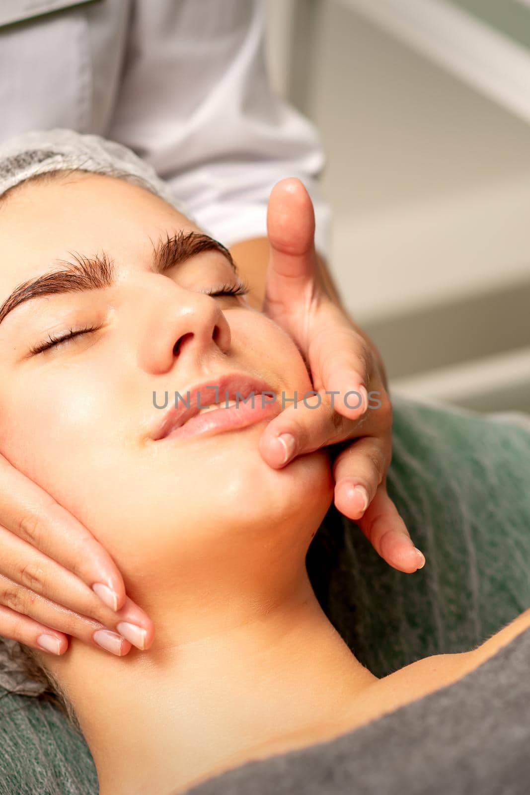 Face massage. Beautiful caucasian young white woman having a facial massage with closed eyes in a spa salon. by okskukuruza