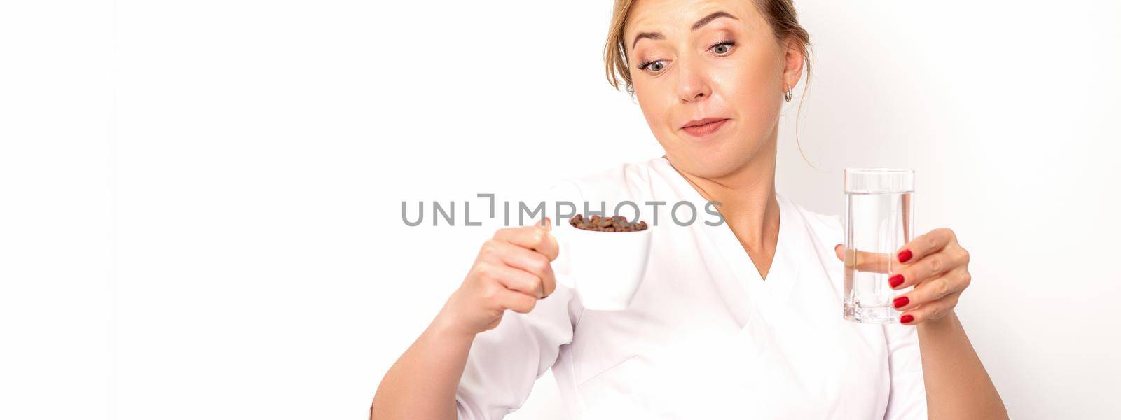 Coffee with water. The female nutritionist holds a cup of coffee beans and a glass of water in her hands on white background