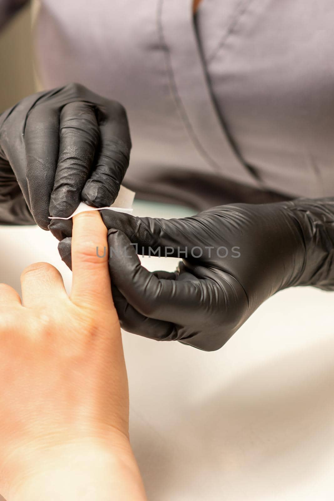 The manicurist finishes the procedure for red nail polishing and cleaning with a cotton napkin, pad, swab in a beauty salon, close up. by okskukuruza