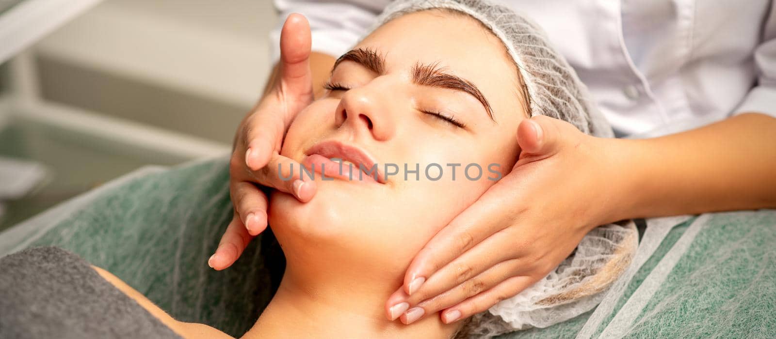 Face massage. Beautiful caucasian young white woman having a facial massage with closed eyes in a spa salon. by okskukuruza