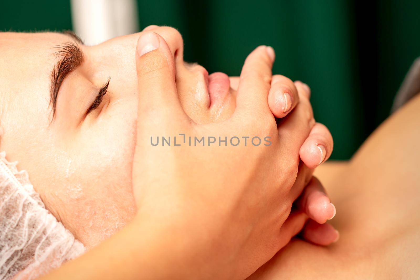 Face massage. Beautiful caucasian young white woman having a facial massage with closed eyes in a spa salon