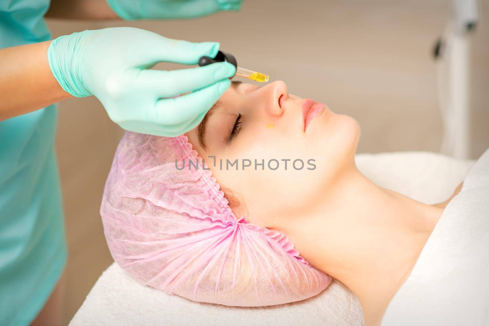 Young white woman getting acid organic retinol peel face skin with the pipette in a beauty clinic. by okskukuruza