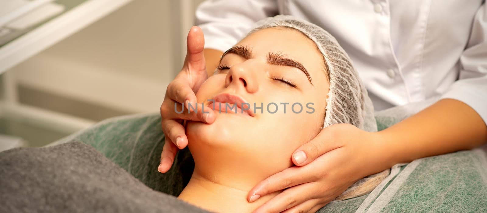 Face massage. Beautiful caucasian young white woman having a facial massage with closed eyes in a spa salon. by okskukuruza