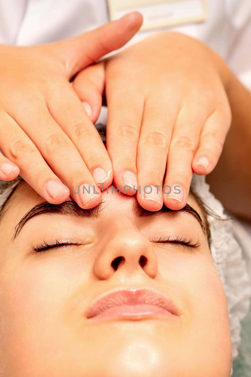 Head massage. Beautiful caucasian young white woman receiving a head and forehead massage with closed eyes in a spa salon