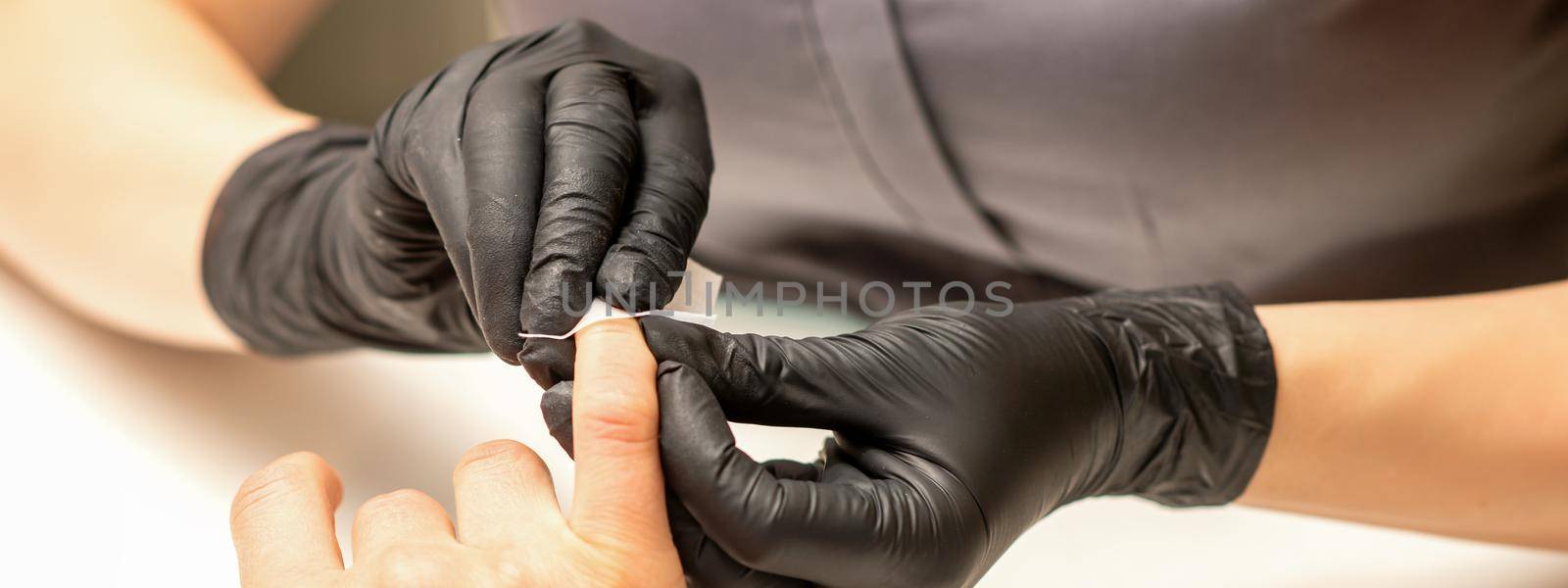 The manicurist finishes the procedure for red nail polishing and cleaning with a cotton napkin, pad, swab in a beauty salon, close up
