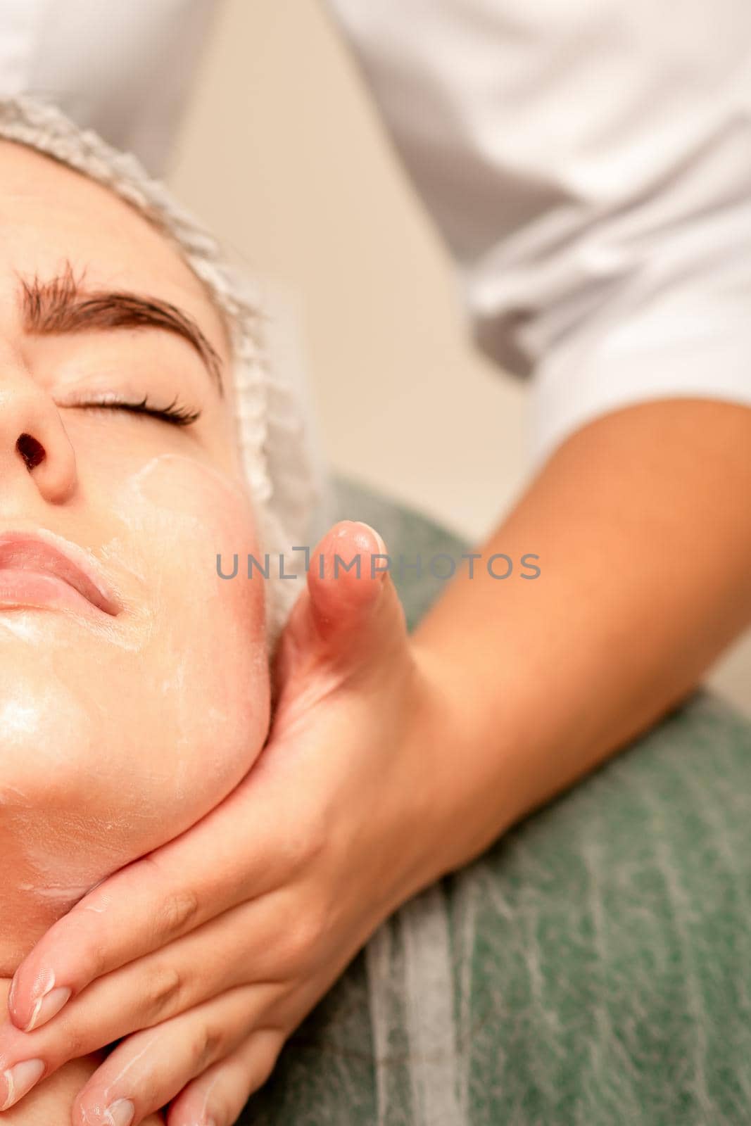 Face massage. Beautiful caucasian young white woman having a facial massage with closed eyes in a spa salon. by okskukuruza