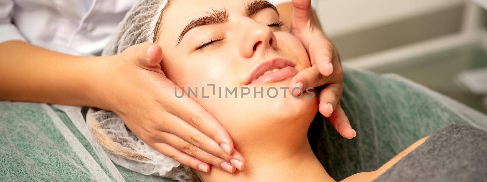 Face massage. Beautiful caucasian young white woman having a facial massage with closed eyes in a spa salon