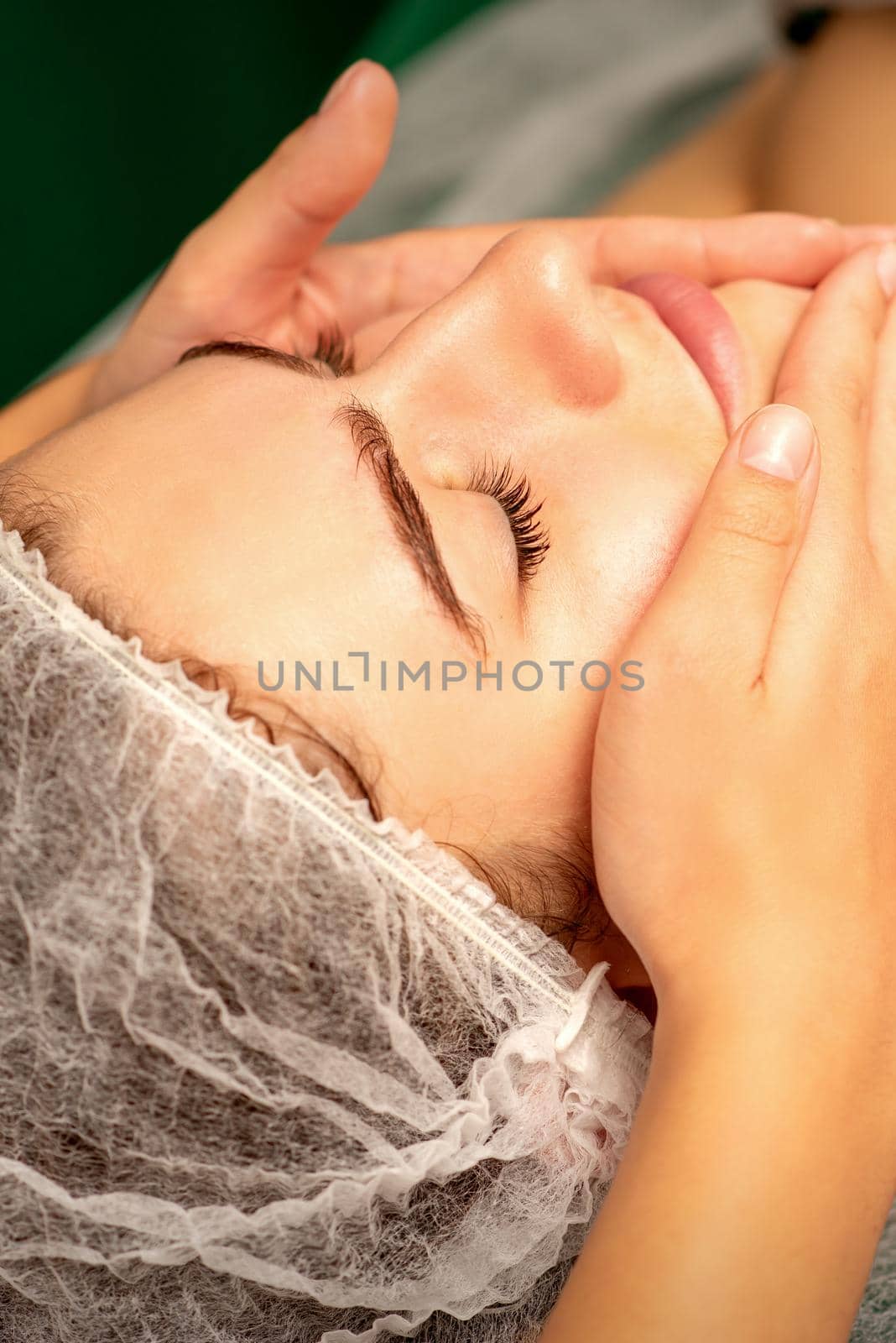 Beautiful caucasian young woman receiving a facial massage with closed eyes in spa salon, close up. Relaxing treatment concept