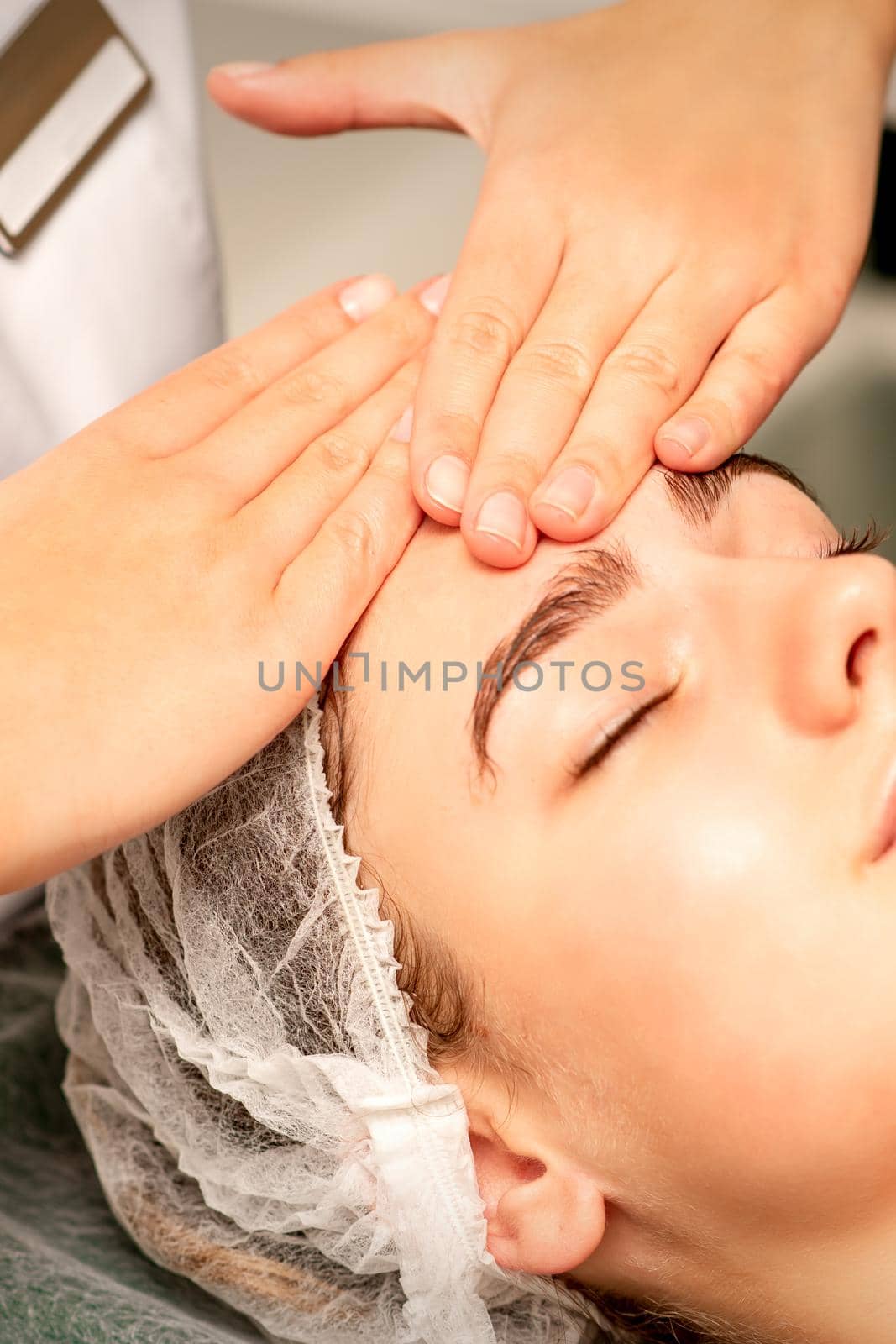 Head massage. Beautiful caucasian young white woman receiving a head and forehead massage with closed eyes in a spa salon