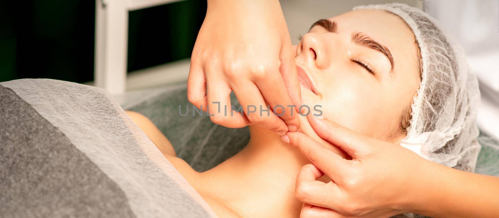 Beautiful young caucasian woman with closed eyes receiving a facial massage in a beauty salon