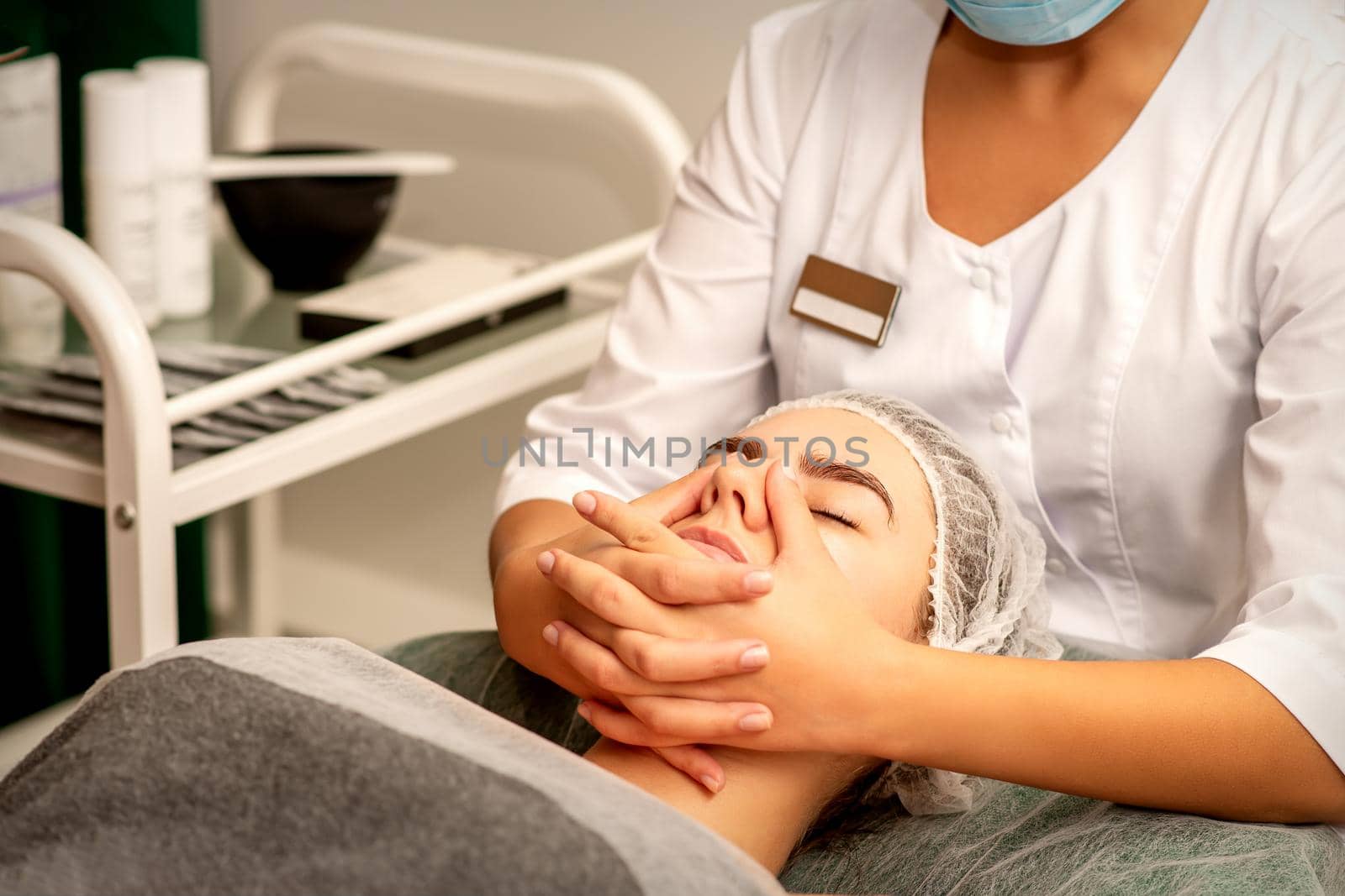 Beautiful young caucasian woman with closed eyes receiving a facial massage in a beauty salon