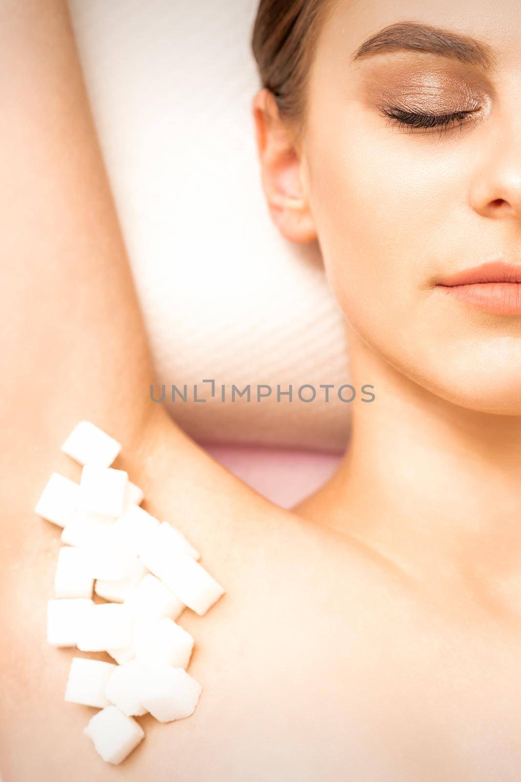 Sugaring, waxing concept. White sugar cubes lie down on the female armpit of the young white woman, close up