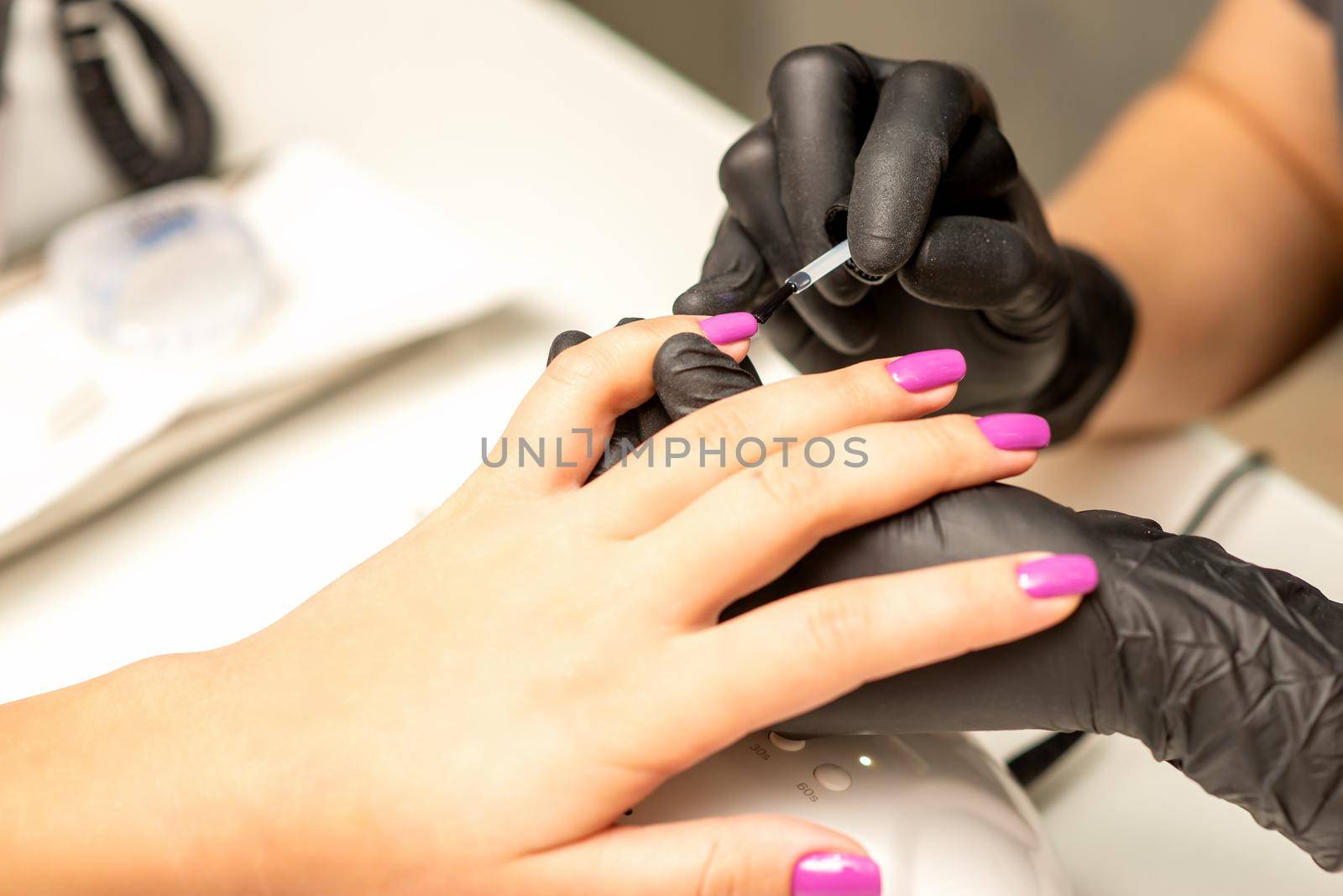 Professional manicure. A manicurist is painting the female nails of a client with purple nail polish in a beauty salon, close up. Beauty industry concept. by okskukuruza