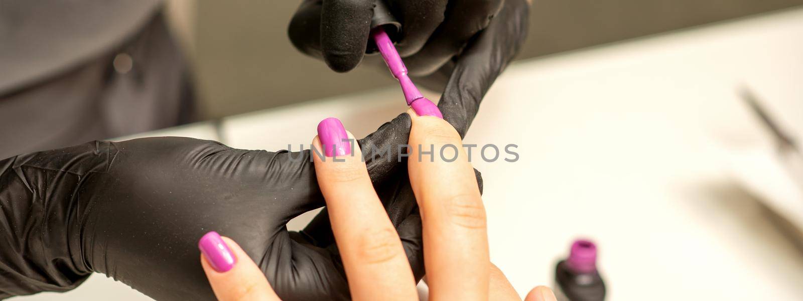 Professional manicure. A manicurist is painting the female nails of a client with purple nail polish in a beauty salon, close up. Beauty industry concept